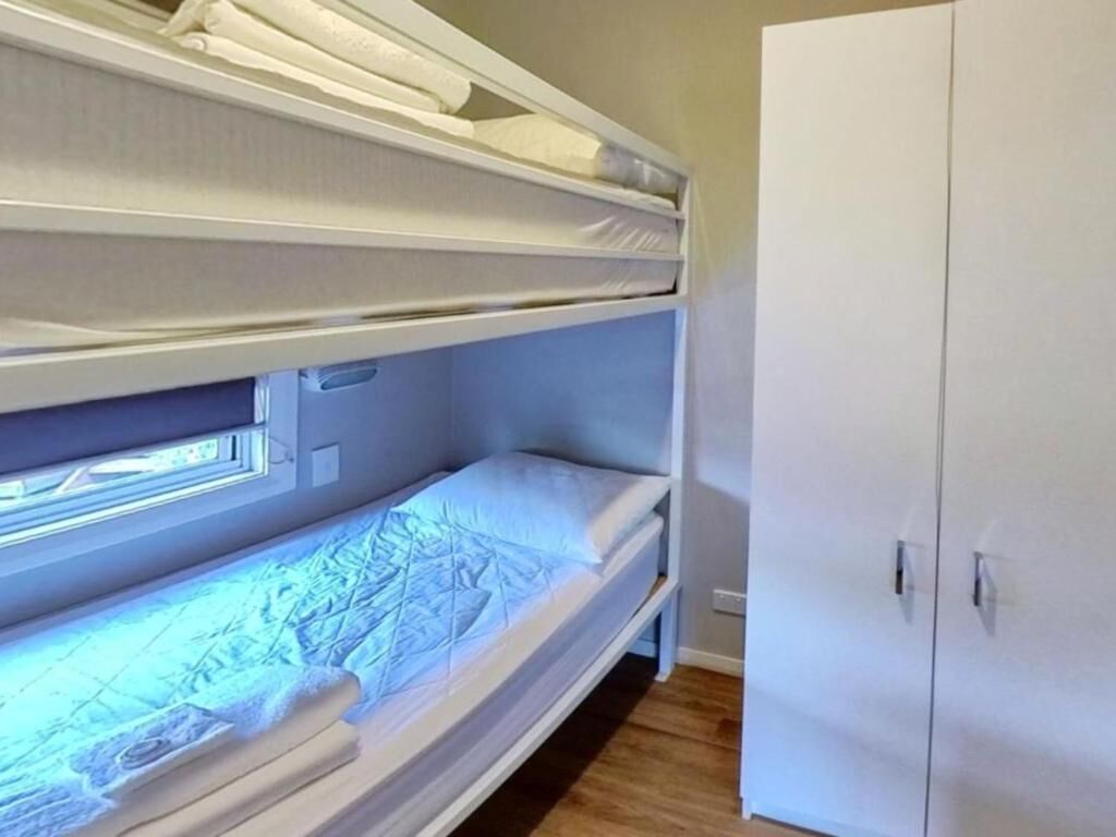 Una cama individual en literas con ventana, un armario y suelo de madera.