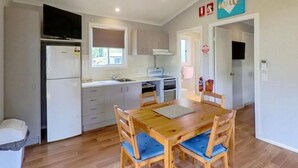 A compact kitchen with a dining table and chairs, a refrigerator, and a microwave. - Camden Holiday Park (Elderslie)