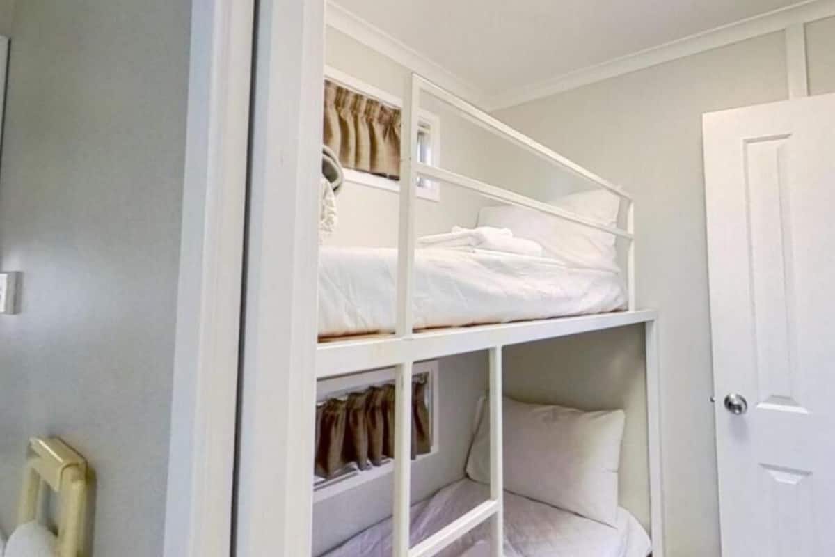 A bunk bed room with a white door and a small window with curtains.