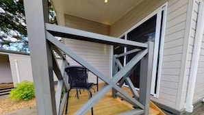 En veranda med en träbänk och en stol, ett metallräcke och ett hus i bakgrunden.