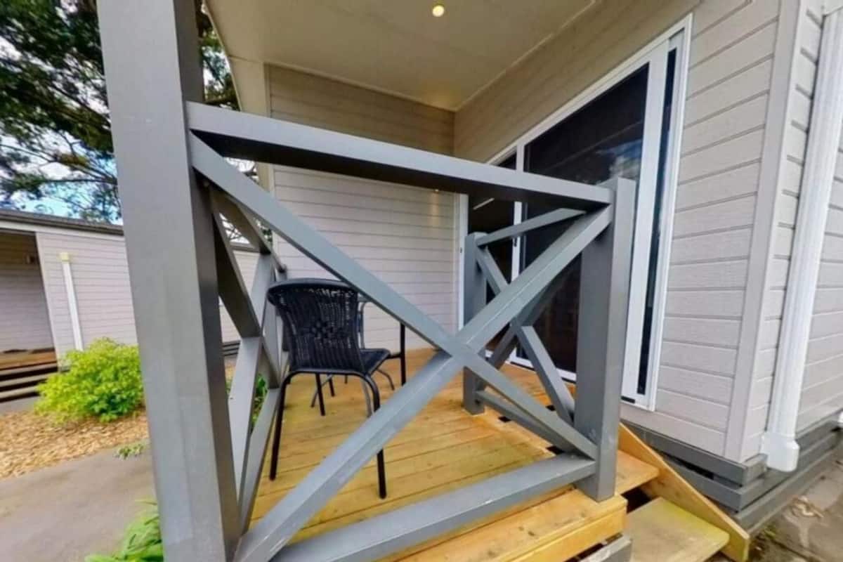 A porch with a wooden bench and a chair, a metal railing, and a house in the background.