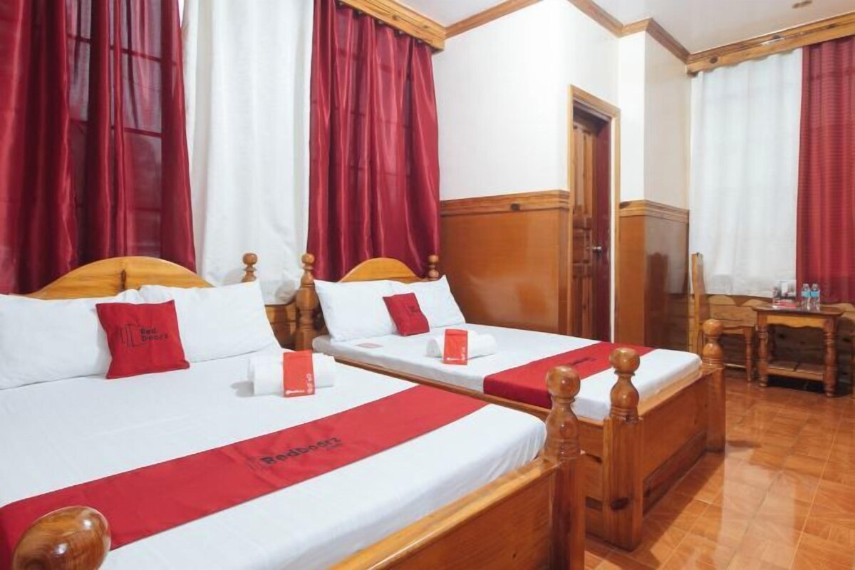 Una habitación de hotel con dos camas de madera, ropa de cama roja y blanca, y un corredor de cama rojo.