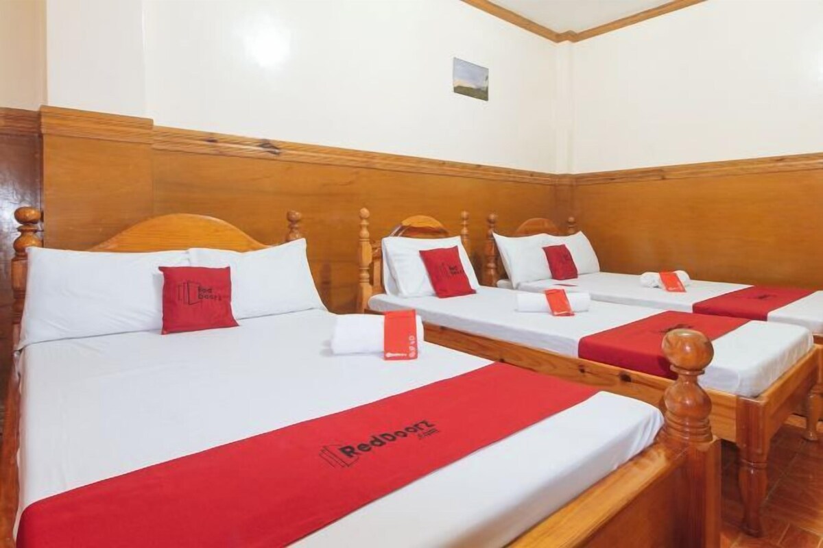 A hotel room with three single beds, each with a red blanket and pillow.