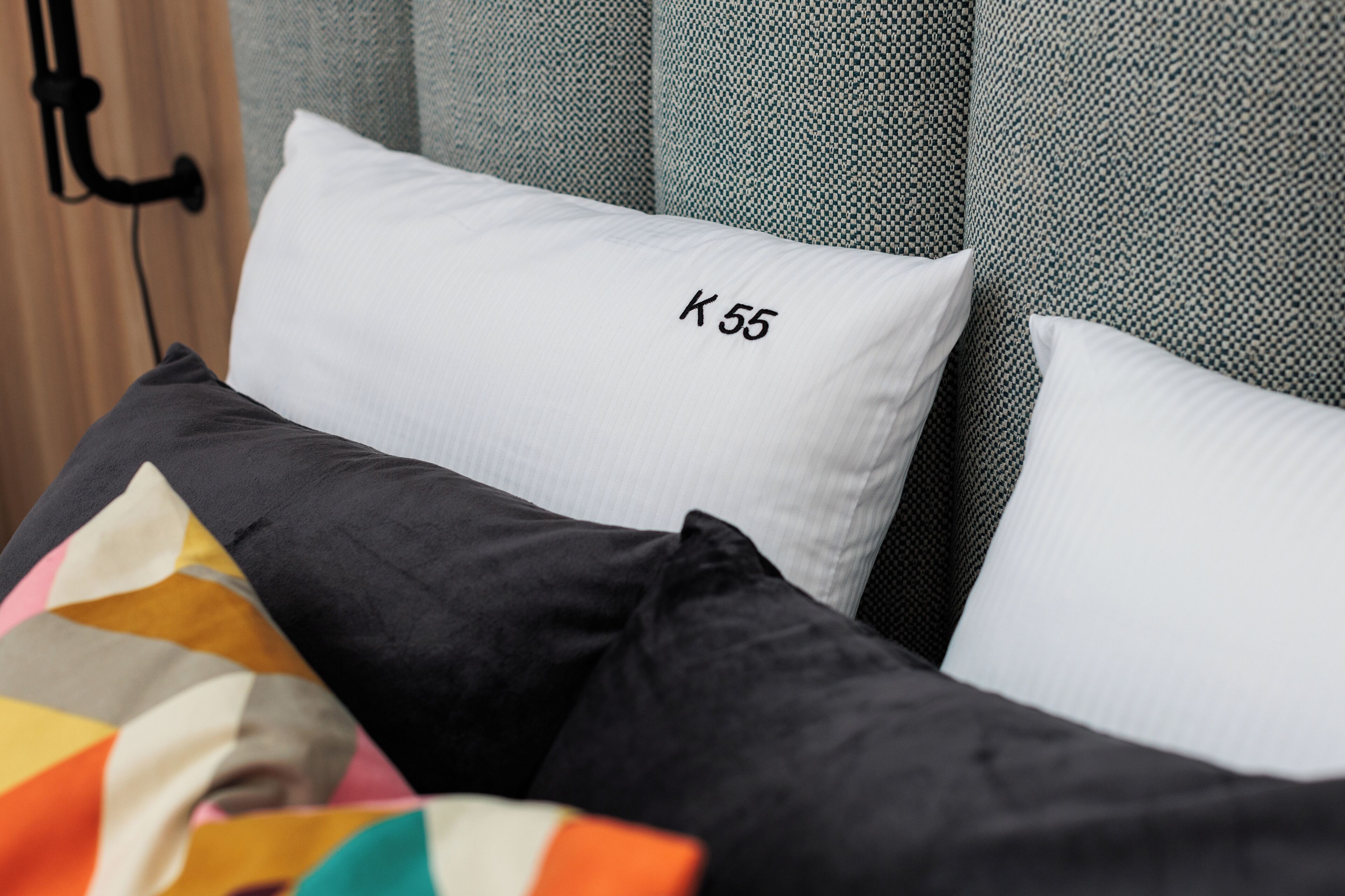 Una cama con almohadas etiquetadas “K 55” y un edredón colorido.