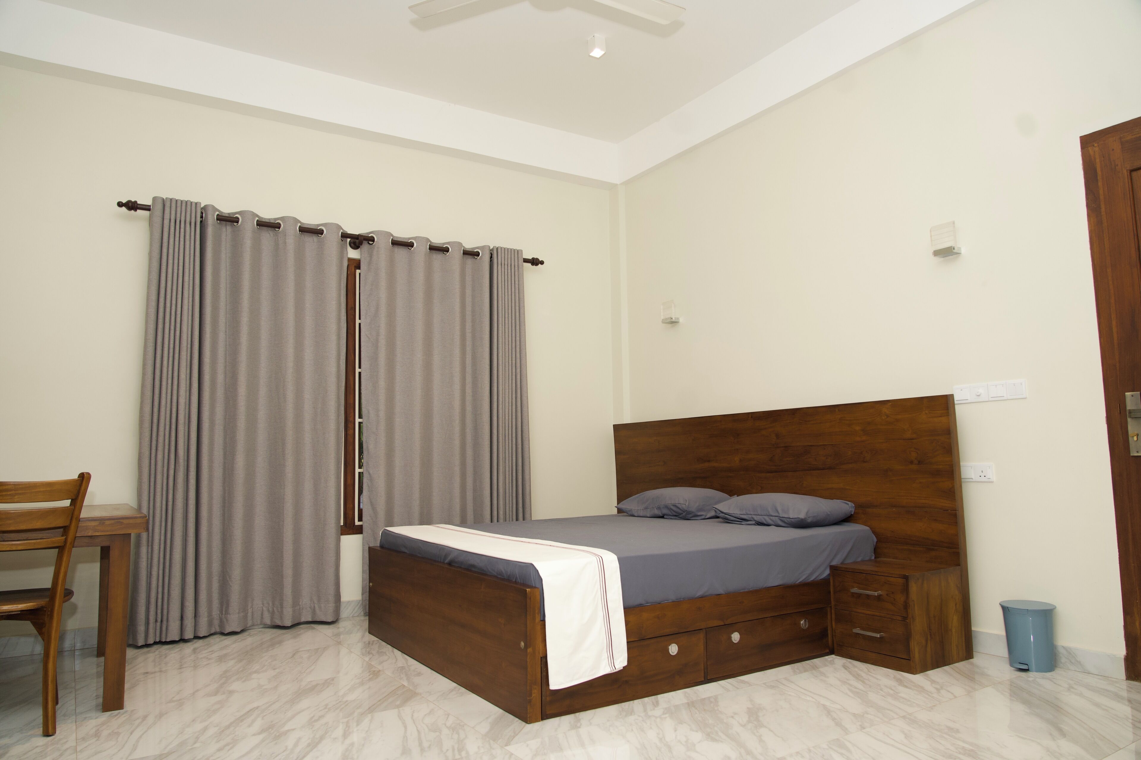 A bedroom with a wooden bed, a bedside table, a chair, and a window with curtains.