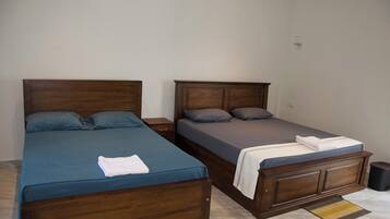 Dos camas de madera con ropa de cama azul y gris, una mesita de noche pequeña y un bote de basura.