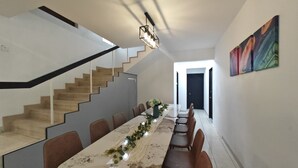 A modern dining area with a long table, brown chairs, a staircase, and a painting on the wall. - Taman Duta KL Deluxe Villa by uBook (Kuala Lumpur)