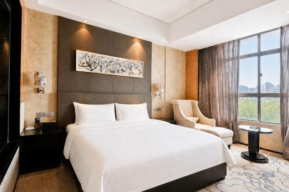 Habitación de hotel con una cama grande, una silla, una mesita y vistas a la ciudad.