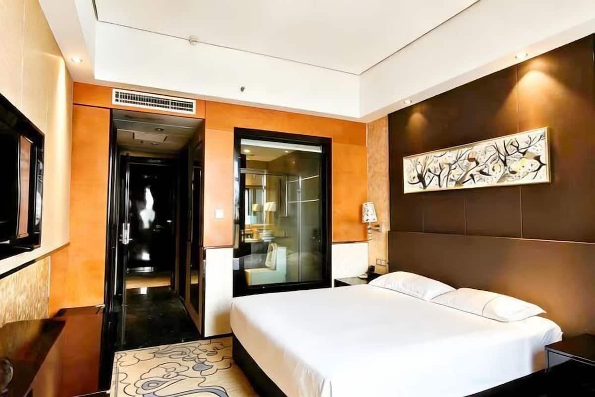 A hotel room with a large bed, a TV, a painting, and a bathroom visible through an open door.