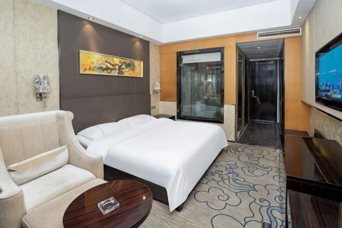 A hotel room with a bed, a sofa, a TV, and a door leading to a hallway.