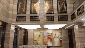 Un hall d’entrée avec un plafond haut, de grandes fenêtres et un espace salon central.