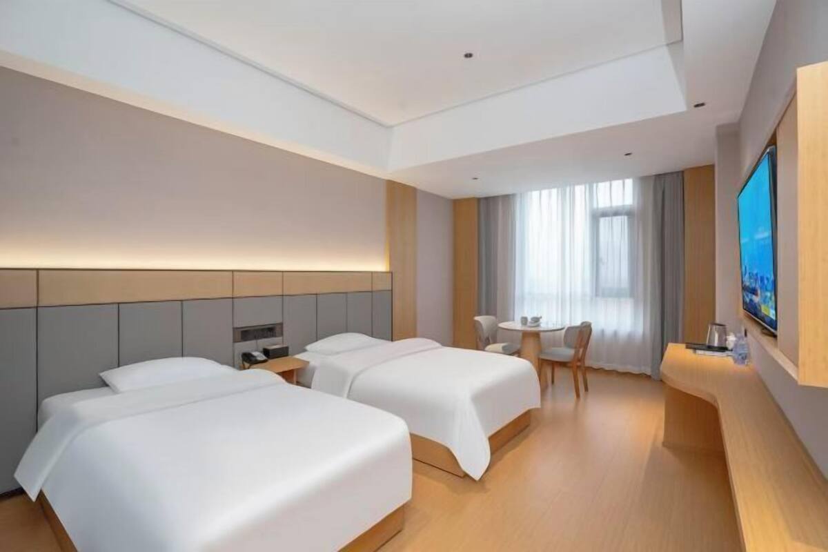 A hotel room with two beds, a desk, a TV, and a window with curtains.
