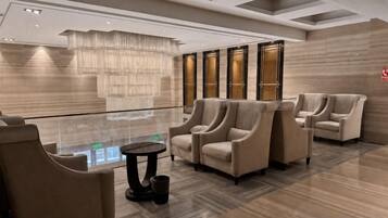 A modern lobby with a chandelier, seating area, and a view of the lobby through a glass partition.
