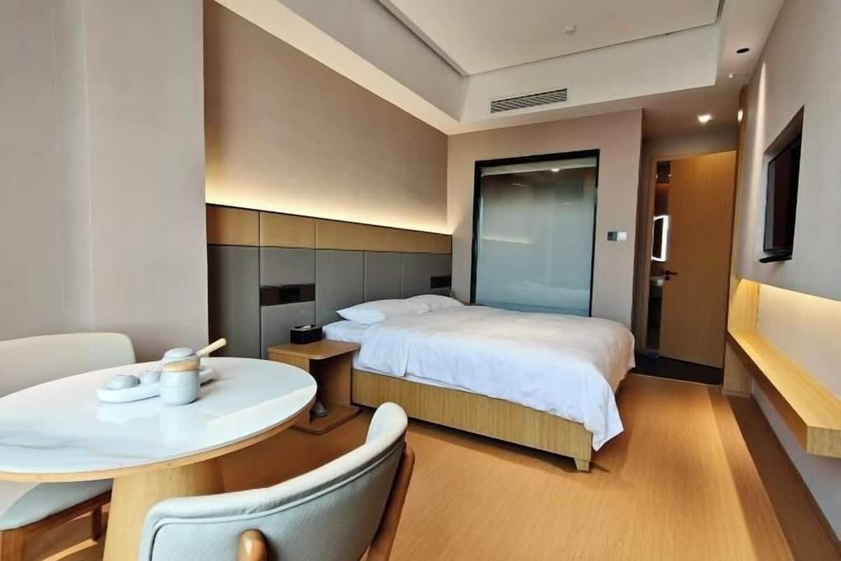 A modern hotel room with a bed, bedside table, and a round dining table with chairs.