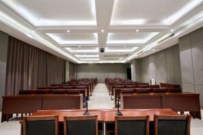 A conference room with rows of wooden tables and chairs, recessed ceiling lighting, and a large screen at the front. - Yilong International Hotel (Xincai Moon Bay Park) (Xincai)
