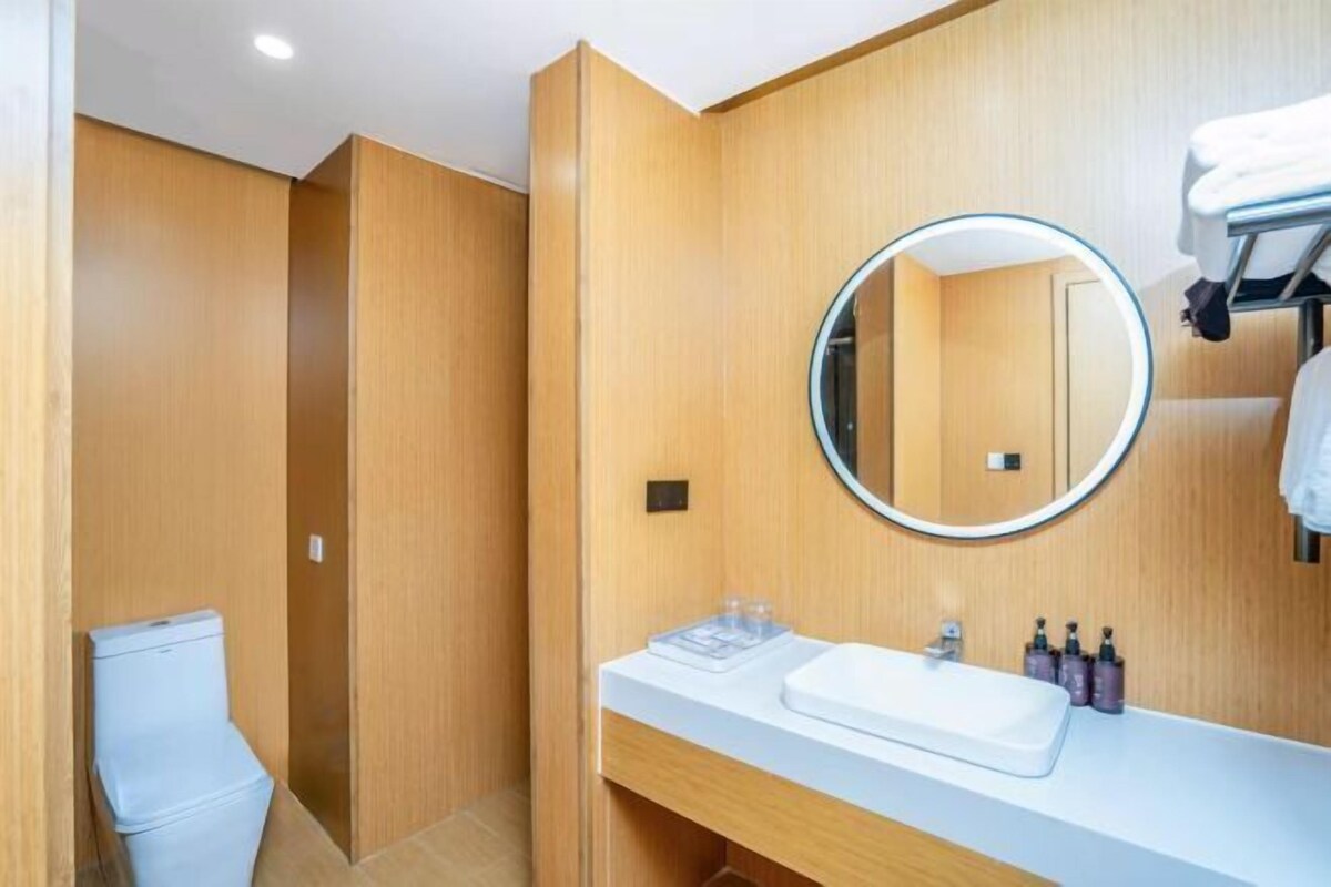 A modern bathroom with a wooden vanity, a round mirror, and a toilet.