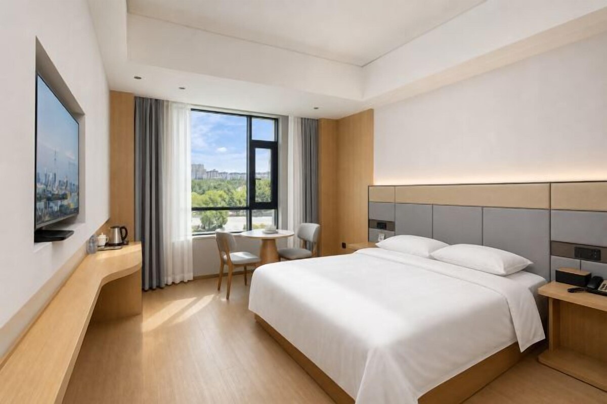 Habitación de hotel con cama, escritorio, silla, televisor y ventana con vistas.