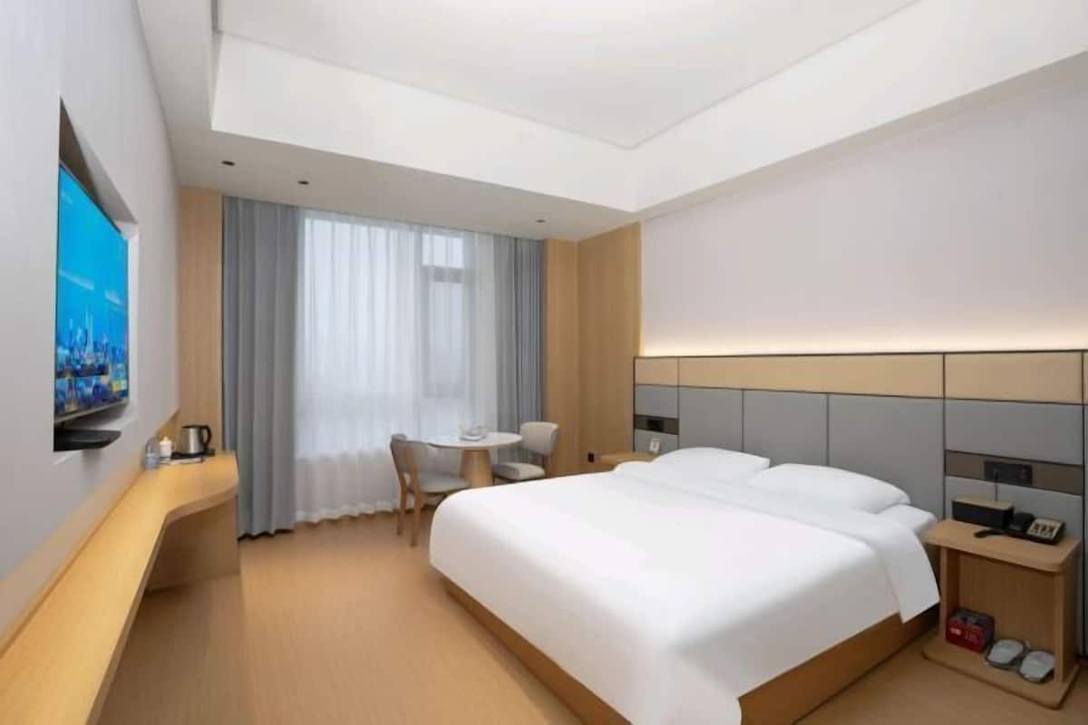 A modern hotel room with a large bed, a desk with a chair, a small table, and a TV mounted on the wall.