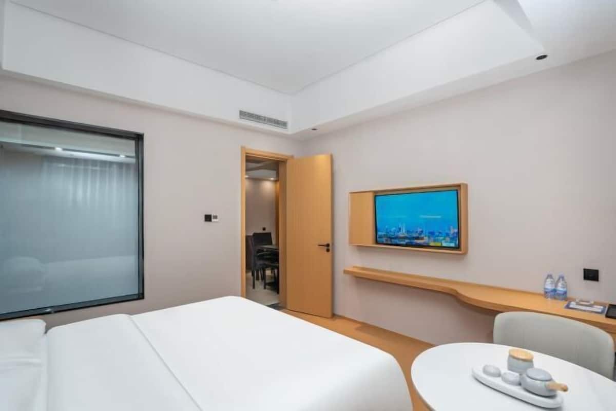 A hotel room with a bed, a TV mounted on the wall, a small table with a tray, and a door leading to another room.