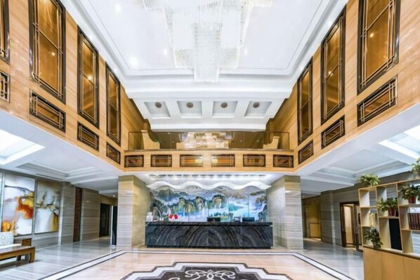 A spacious lobby with a marble floor, a reception desk, and a mural on the back wall. - Yilong International Hotel (Xincai Moon Bay Park) (Xincai)