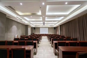 A conference room with rows of wooden tables and chairs, a projector screen at the front, and a ceiling with recessed lighting. - Yilong International Hotel (Xincai Moon Bay Park) (Xincai)