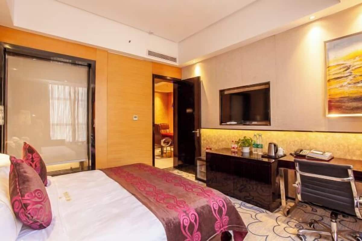 A hotel room with a bed, a desk, a chair, a television, and a painting on the wall.