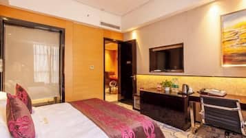 A hotel room with a bed, a desk, a chair, a television, and a painting on the wall.