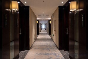 A hotel hallway with doors on both sides, a carpeted floor, and wall-mounted lighting. - Yilong International Hotel (Xincai Moon Bay Park) (Xincai)