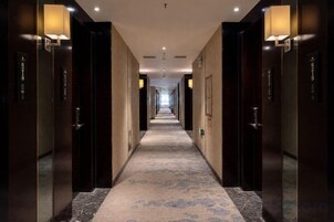 Un pasillo de hotel con puertas a ambos lados, piso alfombrado e iluminación en la pared.
