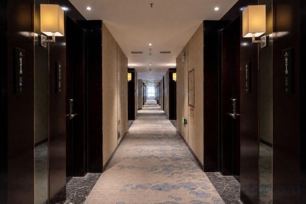 A hotel hallway with doors on both sides, a carpeted floor, and wall-mounted lighting.