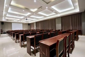 A conference room with rows of wooden tables and chairs, a projector screen, and a large curtain. - Yilong International Hotel (Xincai Moon Bay Park) (Xincai)