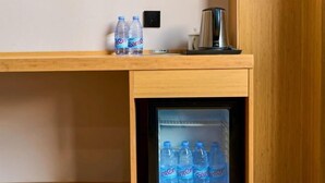 Un comptoir en bois avec deux bouteilles d’eau et une machine à café. En dessous, on trouve un mini-réfrigérateur contenant plusieurs bouteilles d’eau.