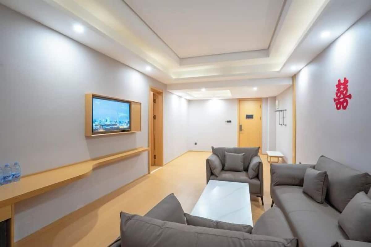 A modern hotel room with a large sofa, a coffee table, and a flat-screen TV mounted on the wall.