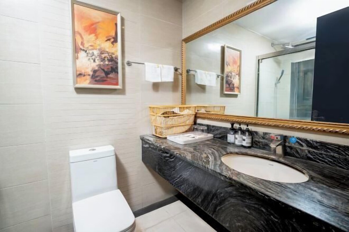 A bathroom with a marble sink, a large mirror, and a toilet. There are towels hanging on a rack and a basket on the counter.