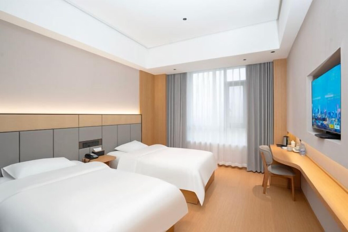 Habitación de hotel con dos camas, un escritorio, un televisor y un ventanal con cortinas.