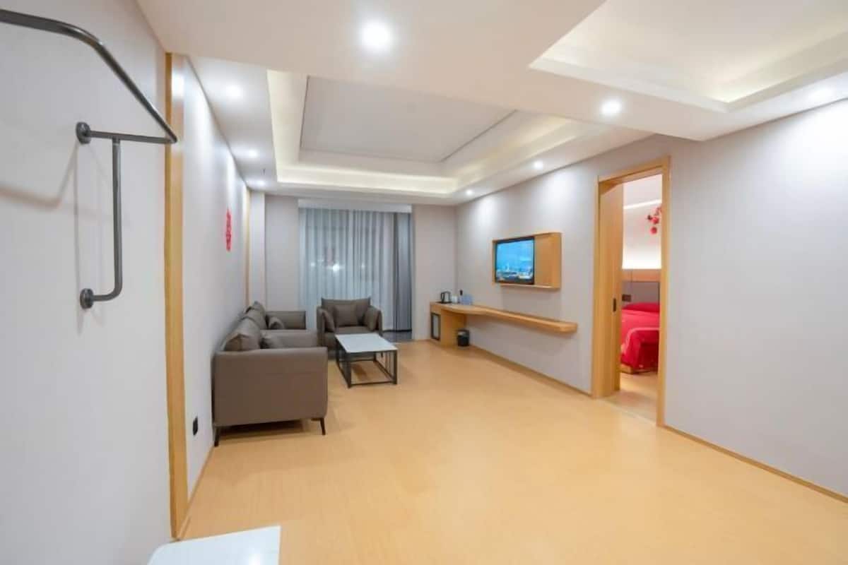 A modern hotel room with a sofa, a small table, a TV mounted on the wall, and a wooden floor.