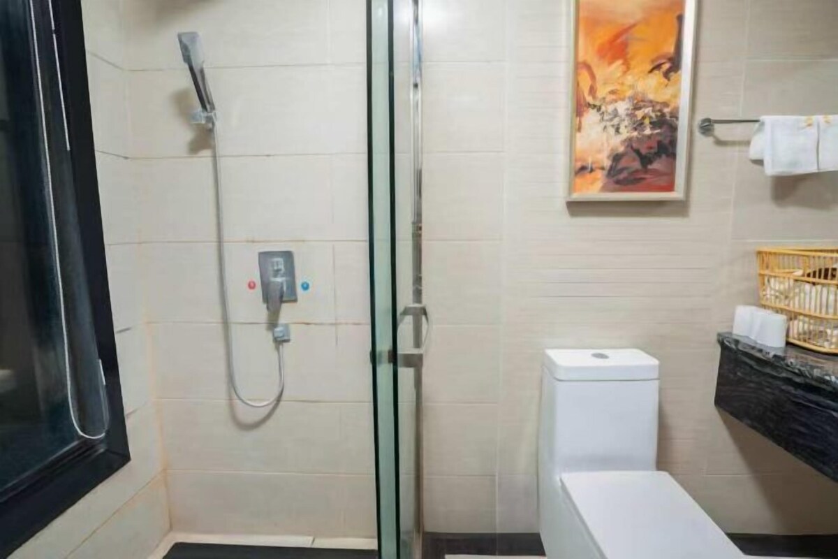 A bathroom with a glass shower enclosure, a white toilet, a marble countertop, and a painting on the wall.