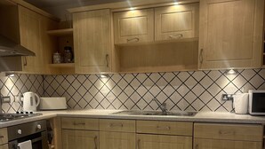 Een keuken met houten kastjes, een betegelde achterwand, een fornuis en een magnetron.
