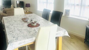 Een eetgedeelte met een tafel gedekt voor vier personen, een bank, een televisie en een raam met uitzicht.