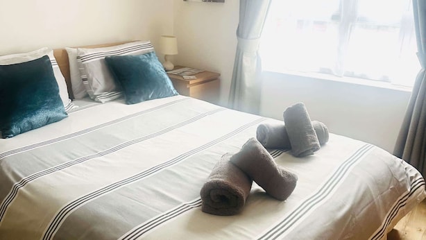 Een net opgemaakt bed met gestreept beddengoed en twee opgerolde handdoeken erop.