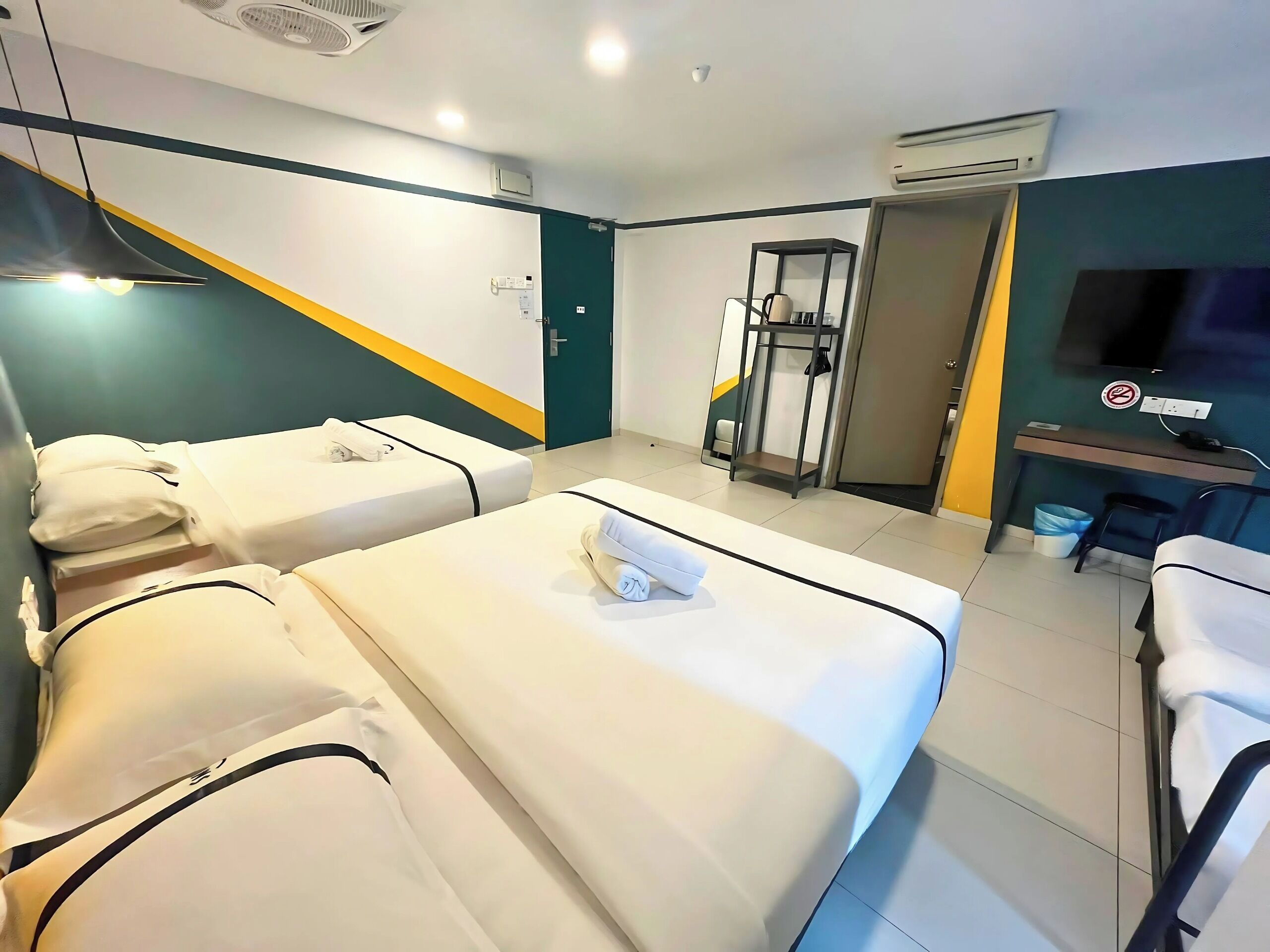 A hotel room with two beds, a TV, a desk, and a gym area.
