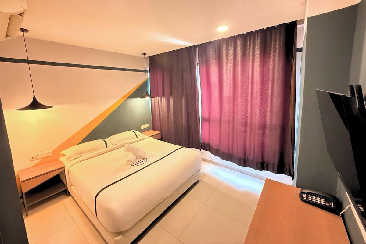 Une chambre d’hôtel moderne, équipée d’un lit, de tables de chevet, d’un bureau avec un ordinateur et une télécommande, ainsi que d’une fenêtre avec des rideaux.