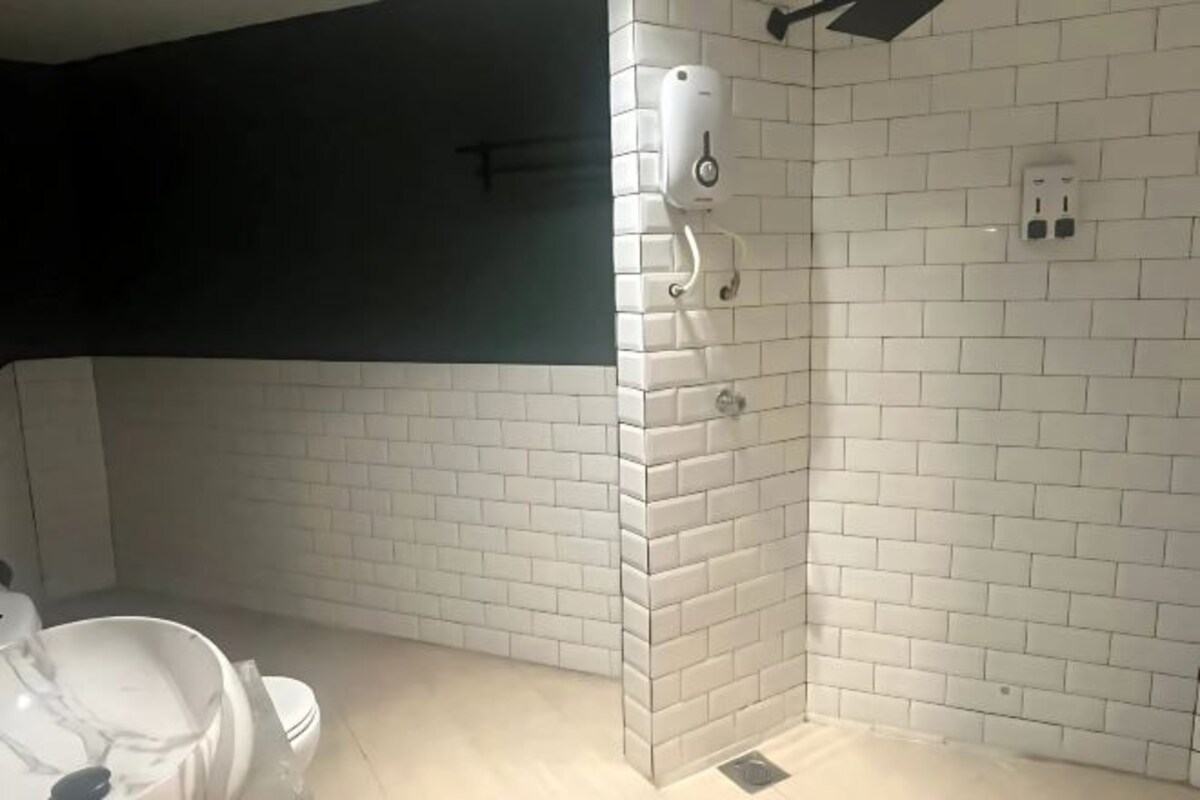 Un baño con azulejos blancos tipo metro, un inodoro, zona de ducha y dispensador de jabón en la pared.