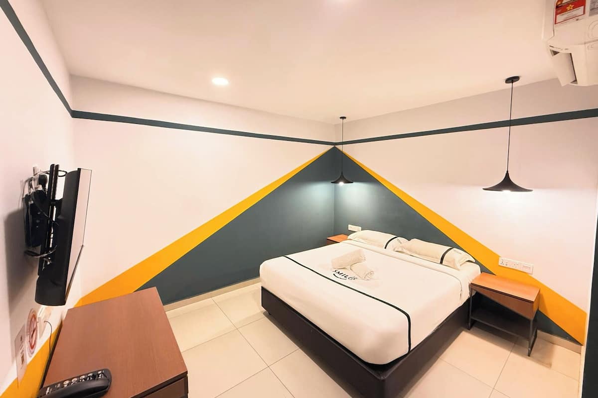 Une chambre d’hôtel équipée d’un lit, d’un bureau, d’une chaise, d’une télévision et d’un radiateur fixé au mur.