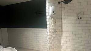 Une salle de bain avec des murs recouverts de carreaux blancs rectangulaires, une douche avec un plafond noir et des toilettes dotées d’un lavabo blanc.