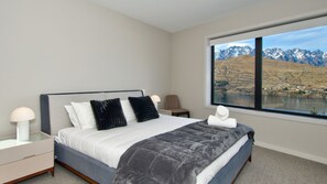 A bedroom with a bed, nightstands, a lamp, a chair, and a large window with a mountain view. - Stunning lake Views from Queenstown townhouse (Queenstown)
