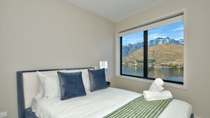 A bedroom with a large bed, a window with a mountain and lake view, and a bedside lamp. - Stunning lake Views from Queenstown townhouse (Queenstown)