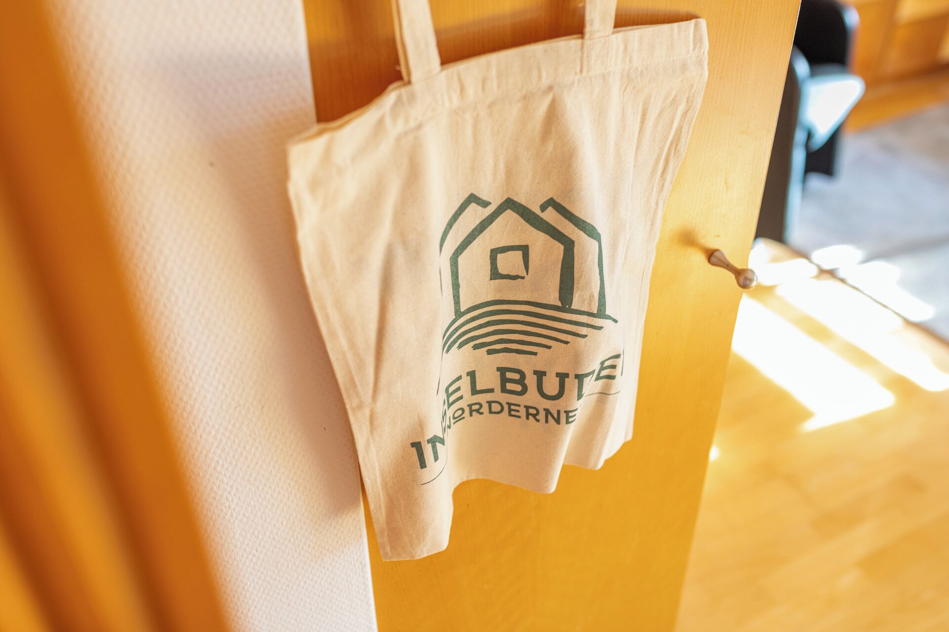 Een witte boodschappentas hangt aan een houten deur, met een logo en tekst.