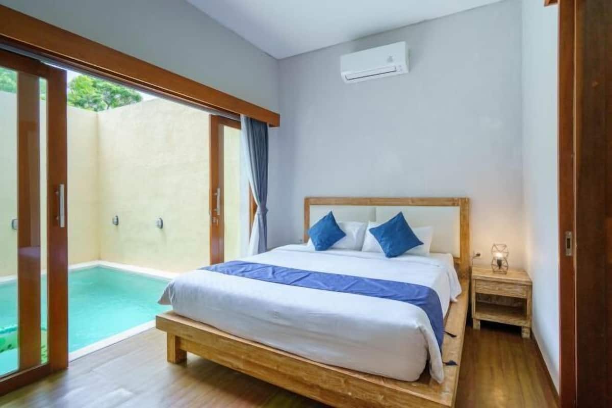 A bedroom with a bed, a nightstand, an air conditioning unit, and a sliding glass door leading to an outdoor area.