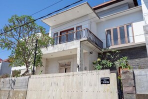 Une maison à deux étages avec un balcon, une entrée fermée par un portail et un mur en pierre.